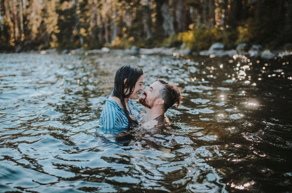 A couple embrace in a lake while smiling at eachother.