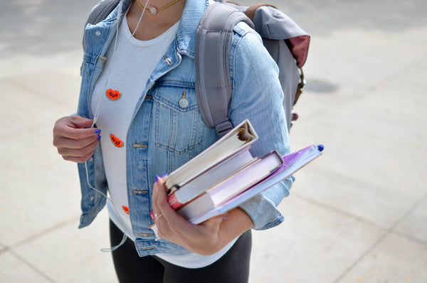 Close up photo of girl wearing headphones and carrying her backpack and textbooks