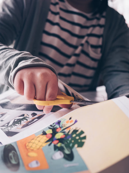 Close up of guy using a pair of yellow scissors to cut through a page in a magazine