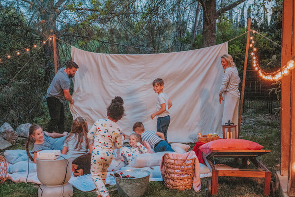 A family gathers around an outdoor tent set up for a outdoor sleepover.