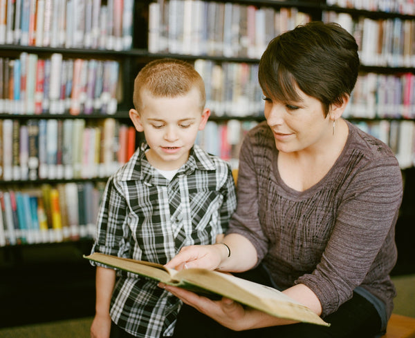Little boy and his teacher reading a book in the library.