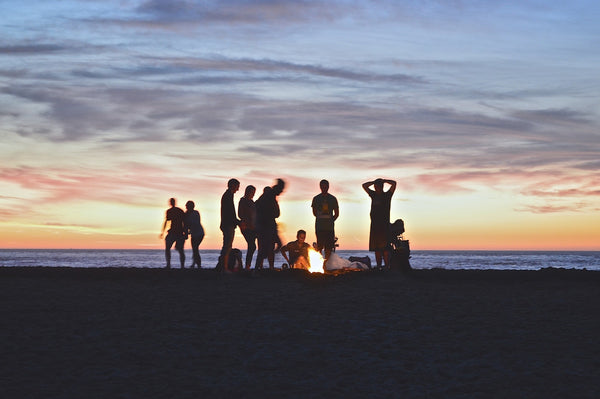 Friends gather around a campfire during sunset