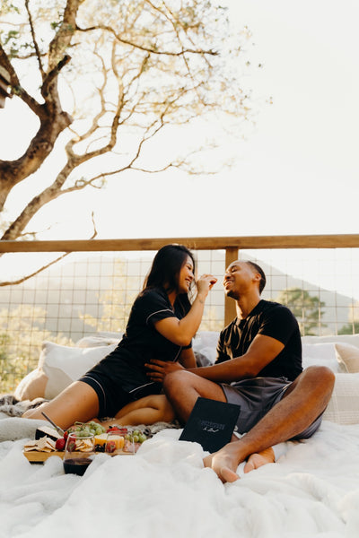 50 Items for Your Sexual Bucket List: Couple enjoying a picnic date outdoors with woman feeding her boyfriend