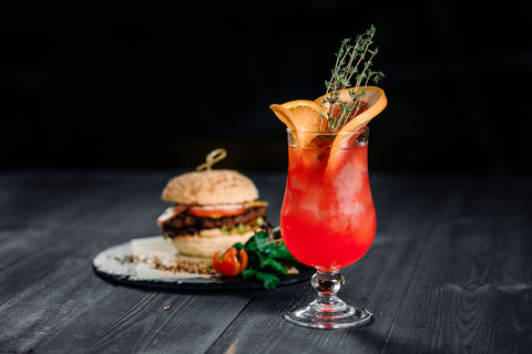 Drink and food. Red citrus cocktail with orange grapefruit and ice with burger on the black wood table