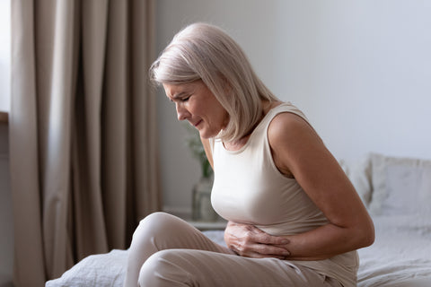 Middle-aged woman sitting on bed feels unhealthy touch stomach suffers from severe crampy abdominal pain, caused by indigestion or diarrhoea, gastric ulcer gastritis problem or unhealthy diet concept