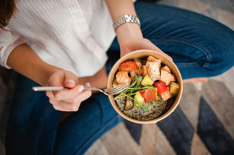 Girl holds a paper plate with healthy food sitting on the floor. Home delivery food. Healthy eating concept. When you stay at home.