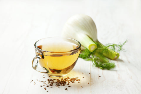 fennel tea in a glass bowl, fresh fennel on a white wooden background