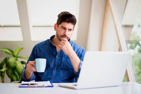 Business man drinking coffee looking at laptop