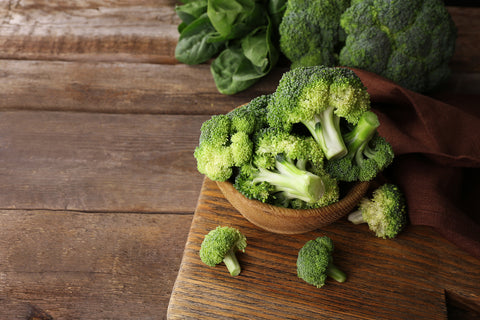 Fresh broccoli with spinach in bowl on wooden table close up