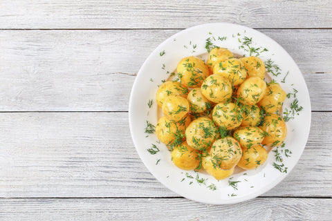 delicious new potatoes sprinkled with finely chopped dill on white plate on table, view from above