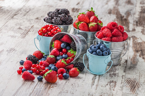 Berries mix blueberry, raspberry, red currant, strawberry, in five old tin cans spilled on white rustic wooden table in studio