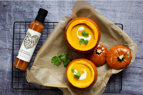 Pumpkin soup served in hollowed out pumpkin bowls with a bottle of Lucy's Dressings on the left 