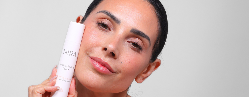 Woman with hydrated skin holding NIRA’s Hyaluronic Acid Serum