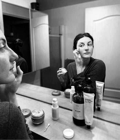 black and white image of a woman applying makeup in the mirror