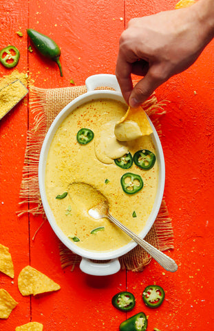 hand dipping corn chip into a casserole dish of vegan queso