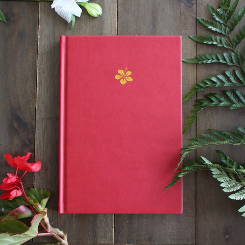 Flowers surrounding a red bullet journal with a gold hibiscus on cover