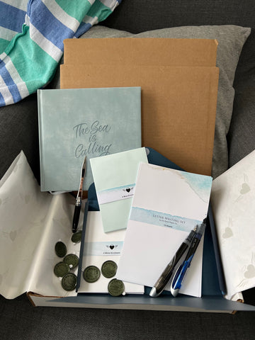 Ocean-themed stationery subscription box displayed on a chair with beach towel