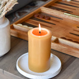 a bees wax pillar candle burning on a coffee table with a board game