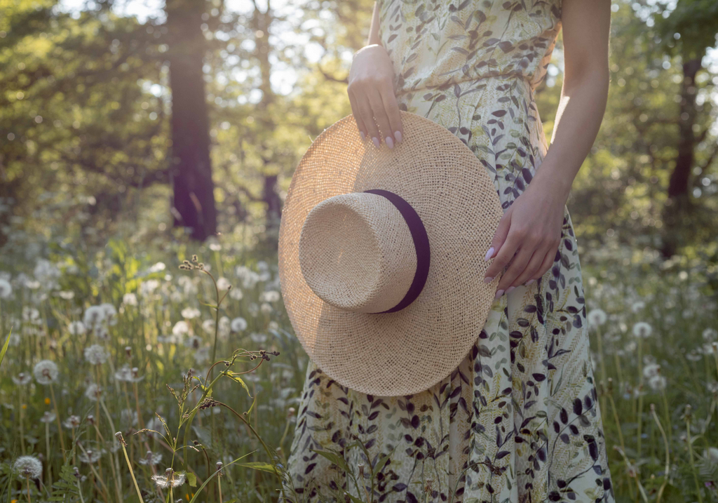 woman wearing a silk olive print dress and a straw hat in the forest