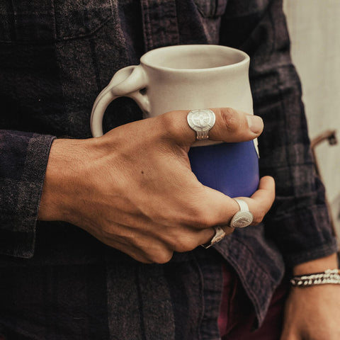 Man holding coffee mug with Air and Anchor jewelry on.