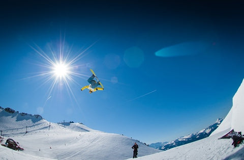 A skiing enthusiast flying off on a snowboard.