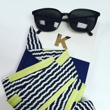 Load image into Gallery viewer, A black, white and neon yellow satin crepe scarf, styled with a notebook and sunglasses on a white background