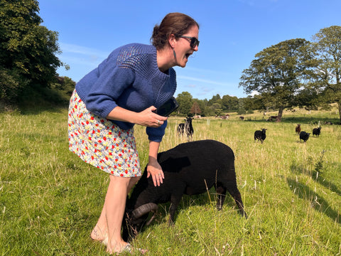 Kate in a field with a sheep nibbling her toes