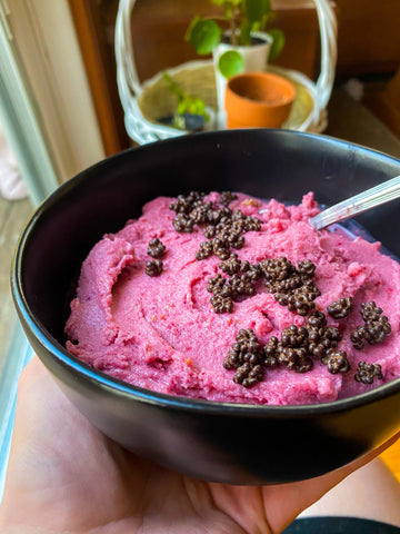 a pink smoothie bowl with chocolate covered cocoa nibs sprinkled on top