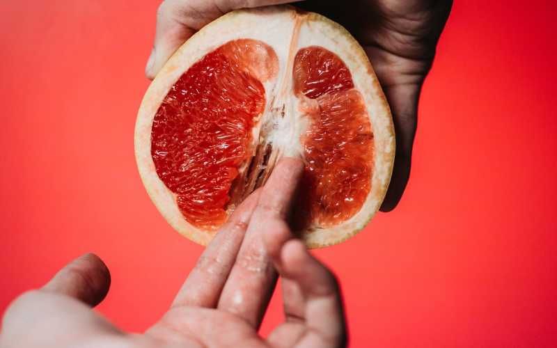 Person holding a sliced grapefruit and entering their fingers into it like a vagina