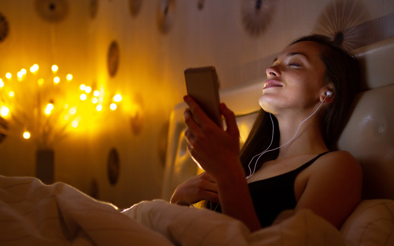 Woman laying in bedroom with lights in the background and headphones in listening to music