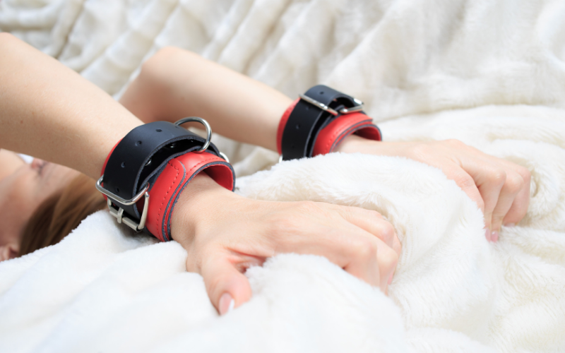 Woman wearing black and red handcuffs grabbing the bed sheets