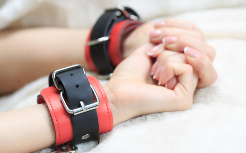 Image of hands pulled back in red and black handcuffs