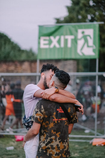 Two men embracing one another outdoors as they kiss