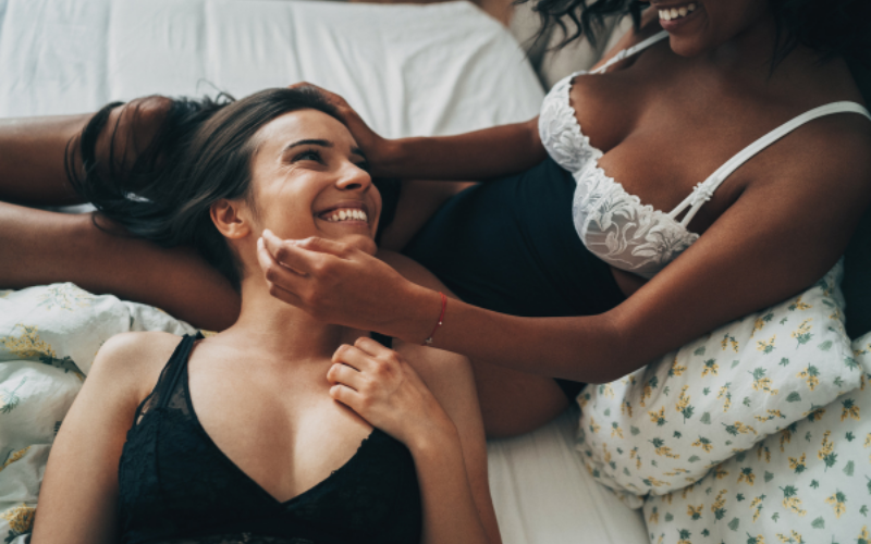 Image of two women in bed in lingerie smiling at one another