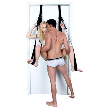 A woman suspended in mid-air using a sex swing while her partner stands in front of her.