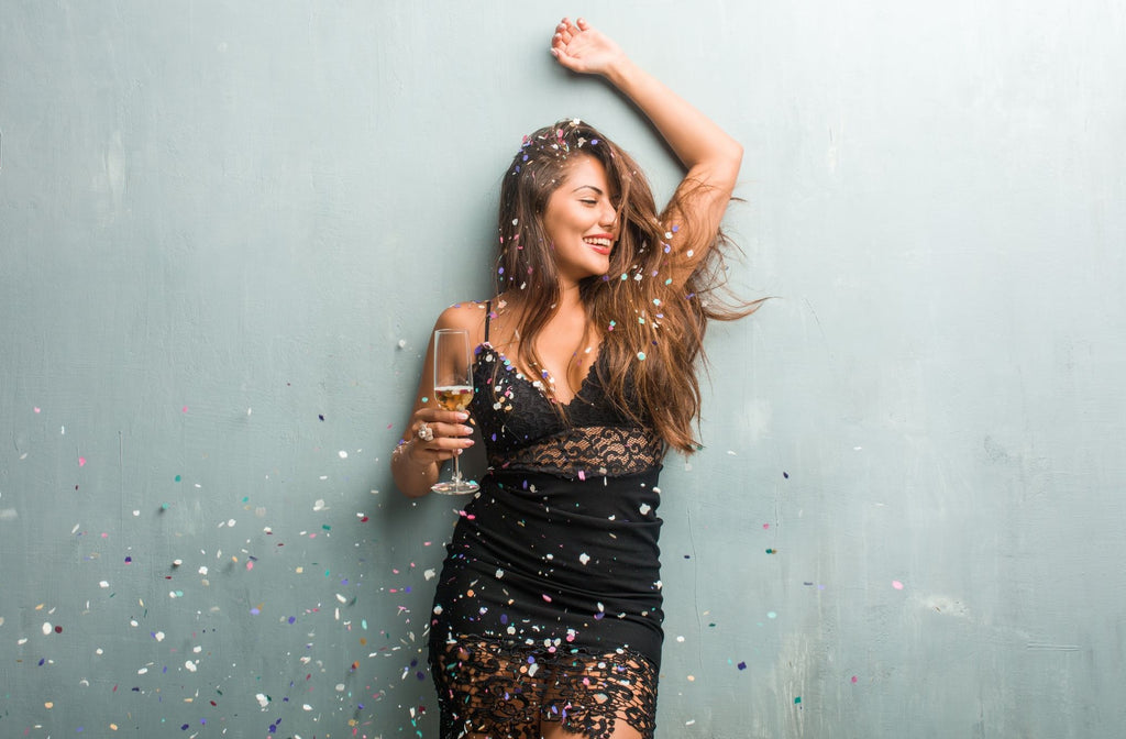 Woman standing with champagne, smiling and confetti falling around her