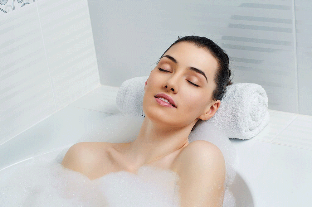 a woman relaxing in a white tub with her head on a towel
