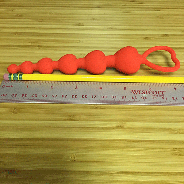 Red heart shaped anal beads next to ruler
