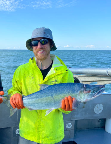 Christian wearing his blue bucket hat and polarized sunglasses while he is holding a fish on the boat.