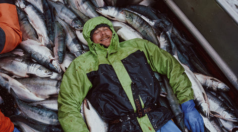 A fisherman in a pile of fish on the boat deck.