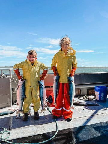 Tommy and Ava in fishing gear on the boat holding a salmon in each hand.