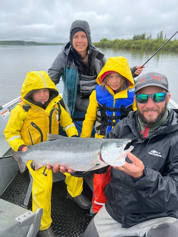 Steve, Jenn and their two children, Ava and Tommy, holding a salmon, kneeling in fishing gear on a boat