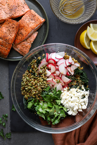 Bowl filled with all of the salad ingredients, salmon in portions on a plate next to the bowl 