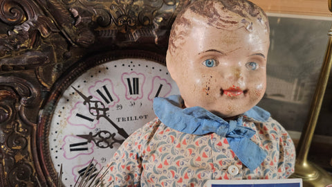 antique comosition doll leaning up against an antique clock