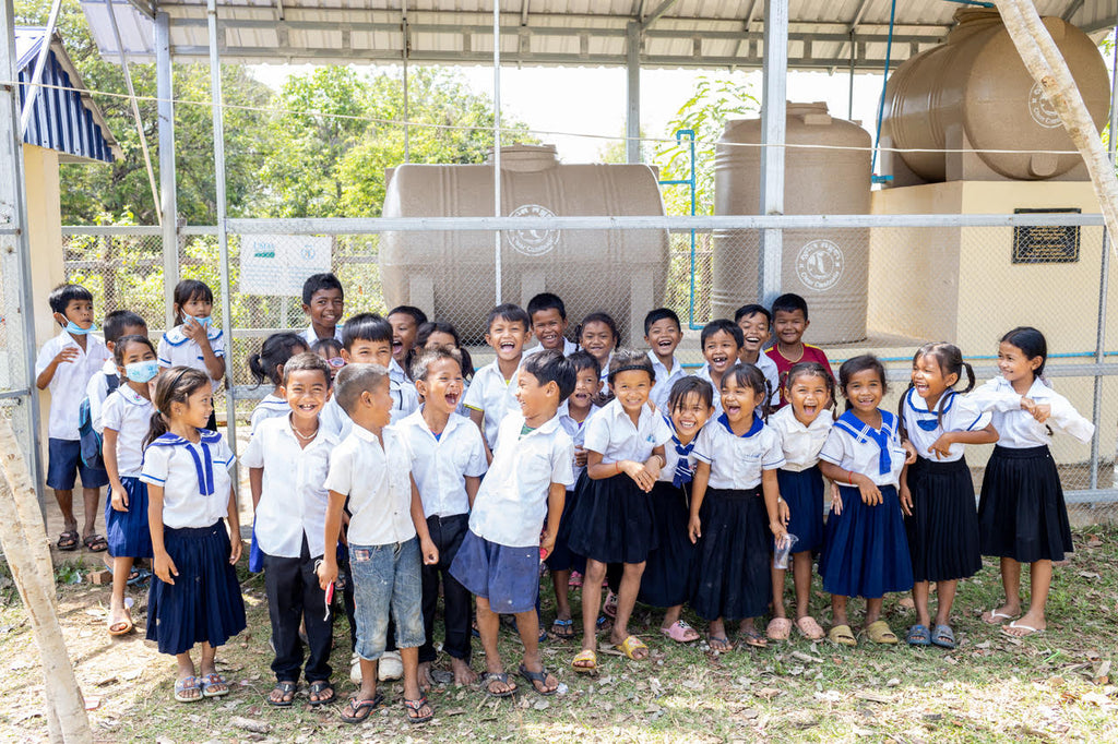 Students stand in front of their school WASH project that provides clean drinking water faucets at school in rural Cambodia.