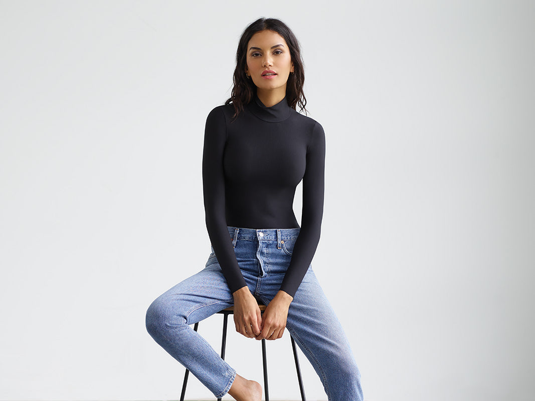 Woman sitting on stool wear Butter Turtleneck Bodysuit and blue jeans 