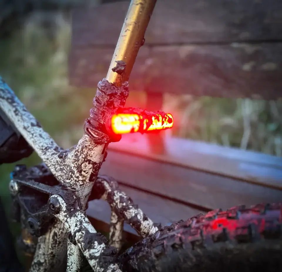 Feu arrière rouge illuminé sur un vélo boueux à la tombée de la nuit.