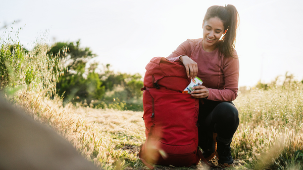 Woman crouching in a field grabbing BOLT energy chews from her backpack