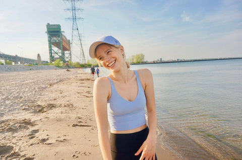 Girl with white ponytail hat smiling at beach with lake water and sand and a bridge behind her