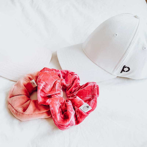 White ponyback ponytail hat with p logo on side with pink scrunchies beside it on a white sheet